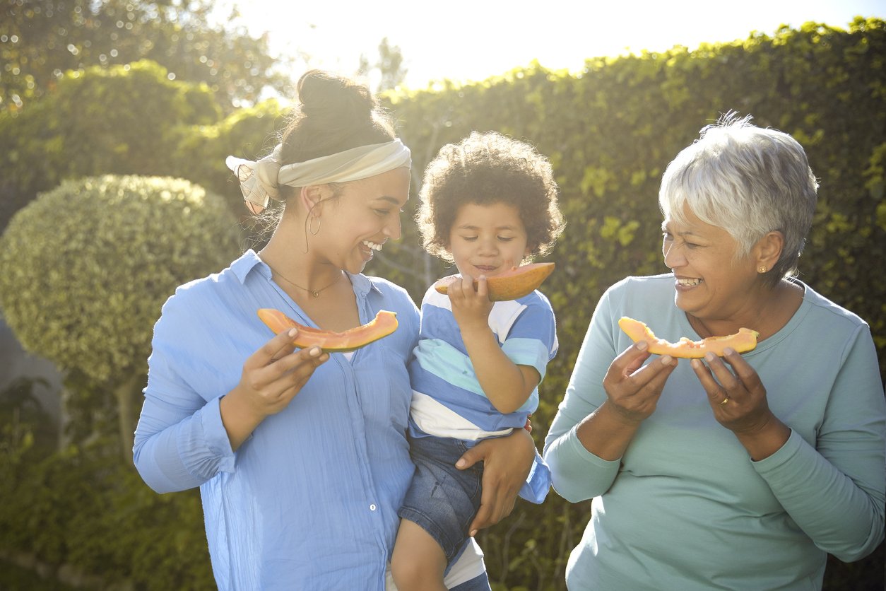 Three generations. Mom, son and grandmother. Enjoying some papaya on a sunny spring day in their garden at home.