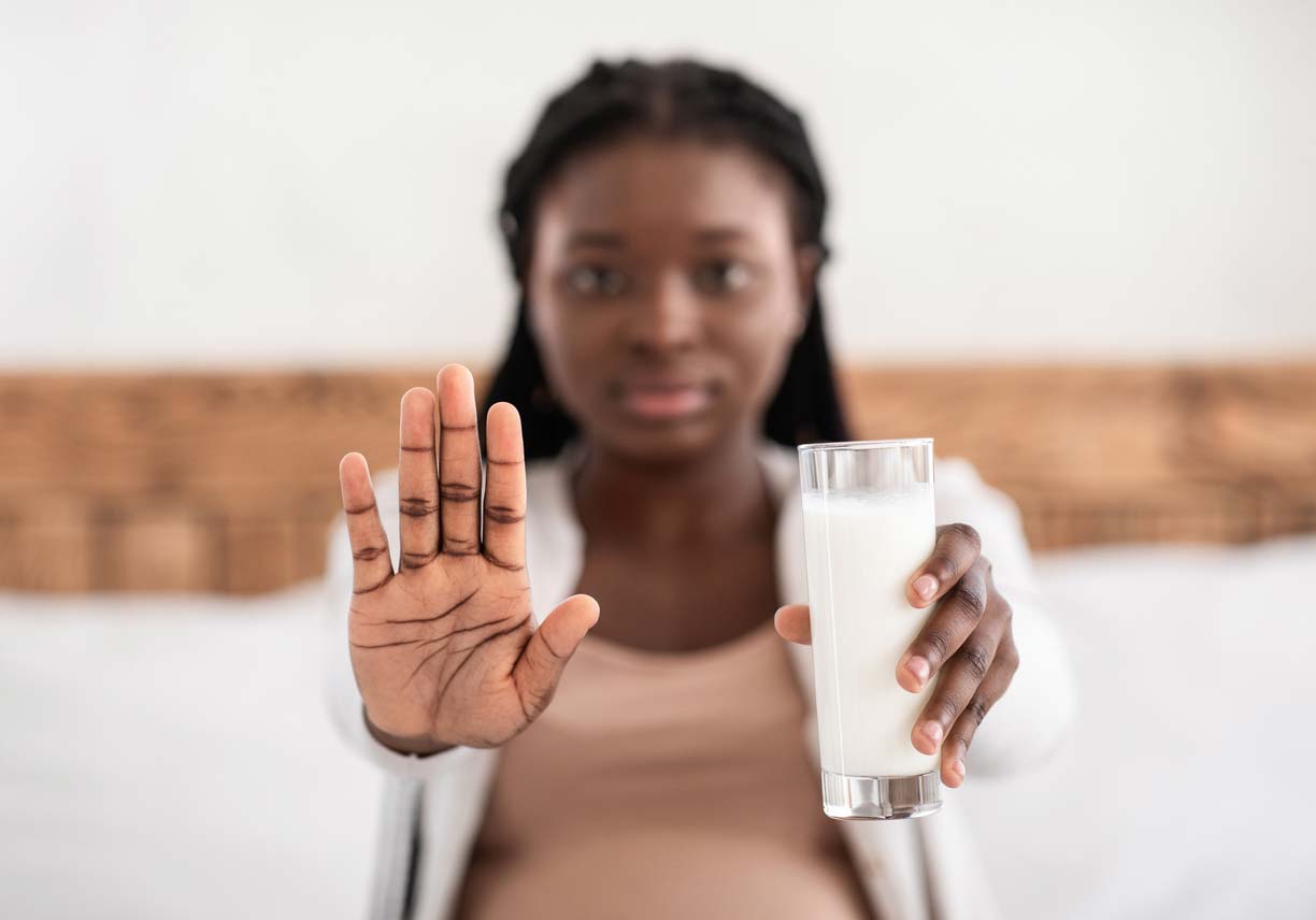 pregnant Black woman holding glass of milk with stop hand gesture