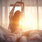 Woman stretching in bed facing window
