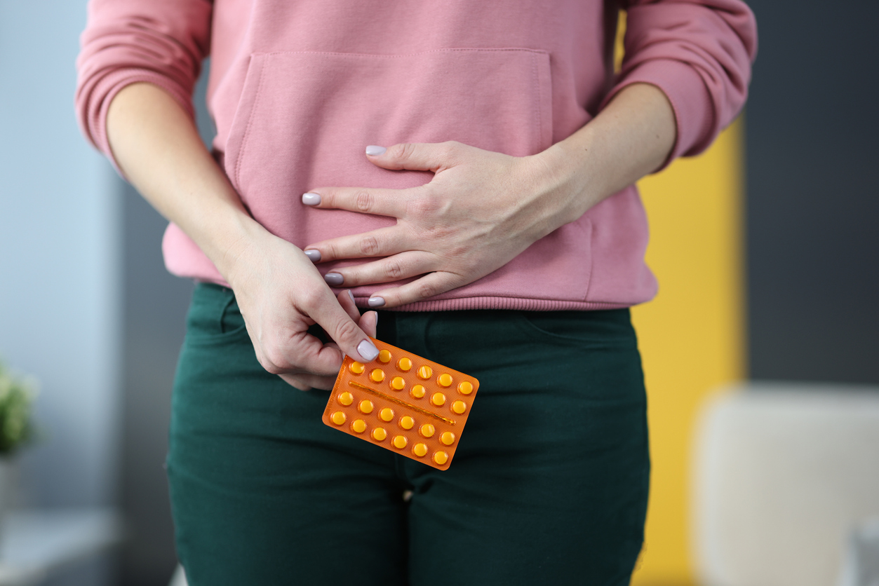 Woman with pills in hands holding lower abdomen