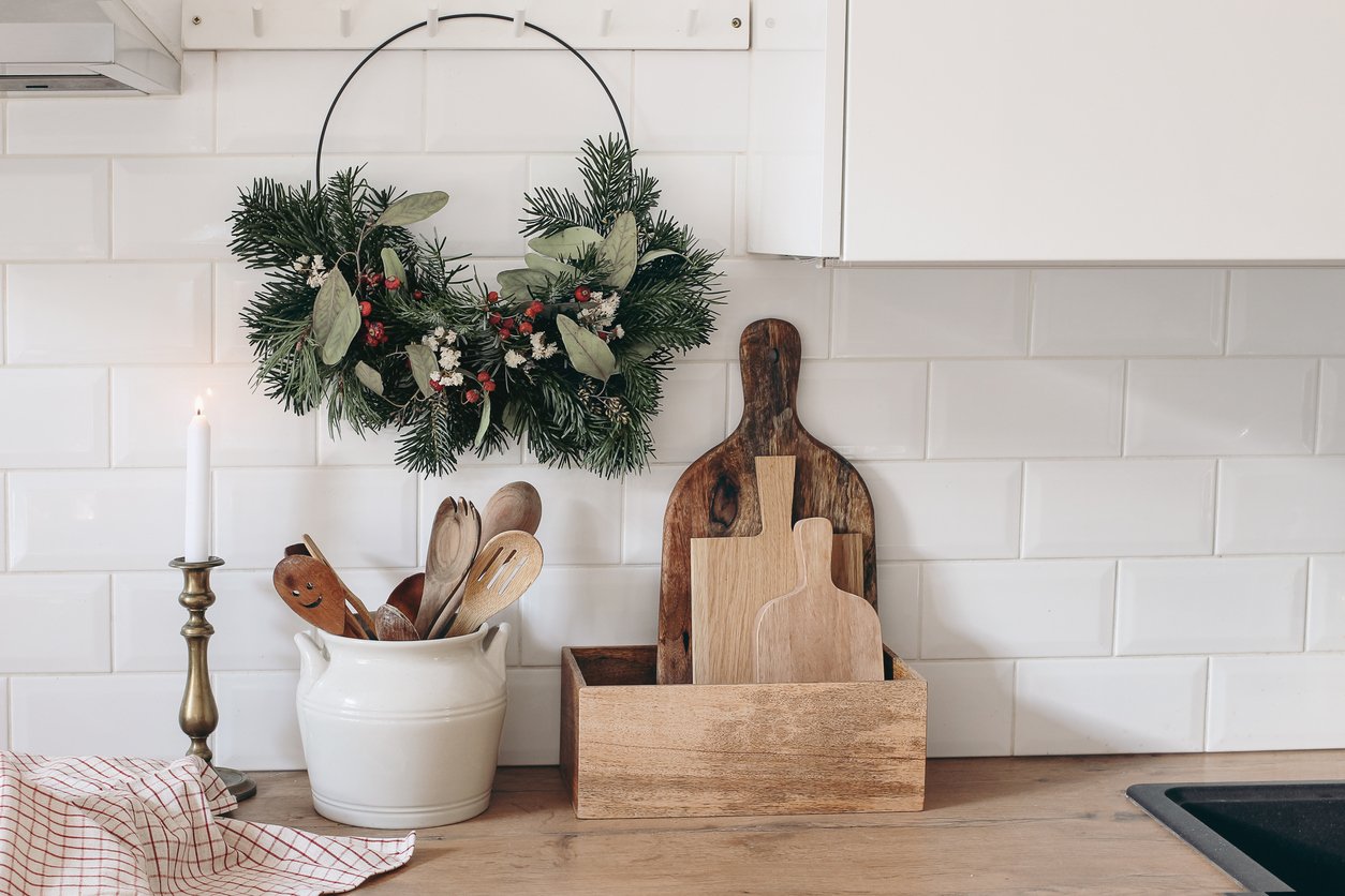 Closeup of kitchen interior. Christmas decoration. Advent floral hoop wreath hanging on peg rails. White brick wall, metro tiles, wooden countertops with kitchen utensils. Vintage scandinavian design.