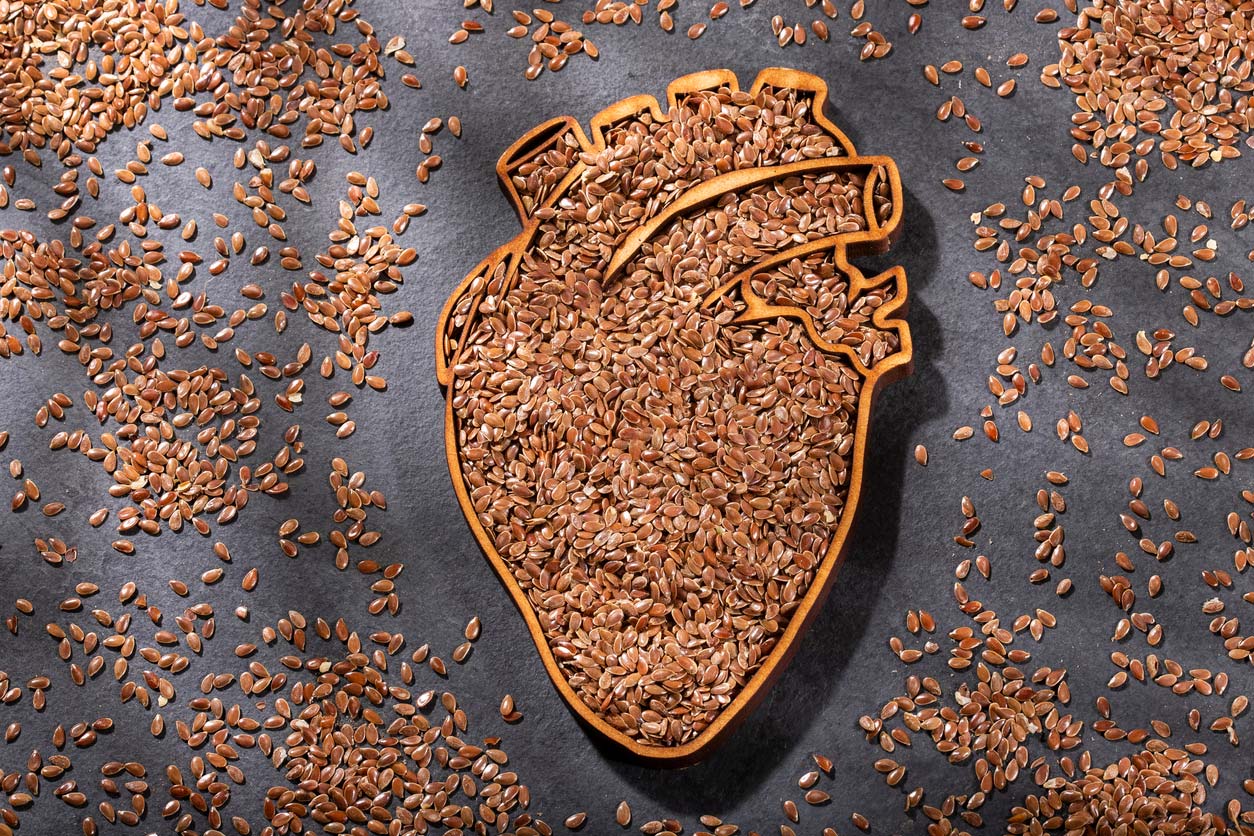 flaxseed all over a table and in an anatomical heart-shaped dish