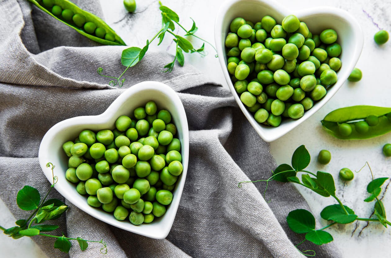 two heart shaped white bowl of green peas