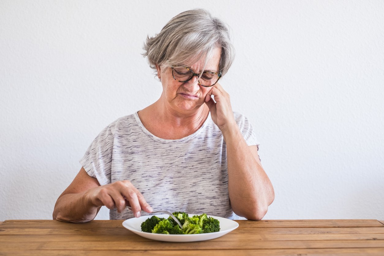 one senior and mature woman dieting and eating healthy looking with disgust face at the broccolis on the wooden table