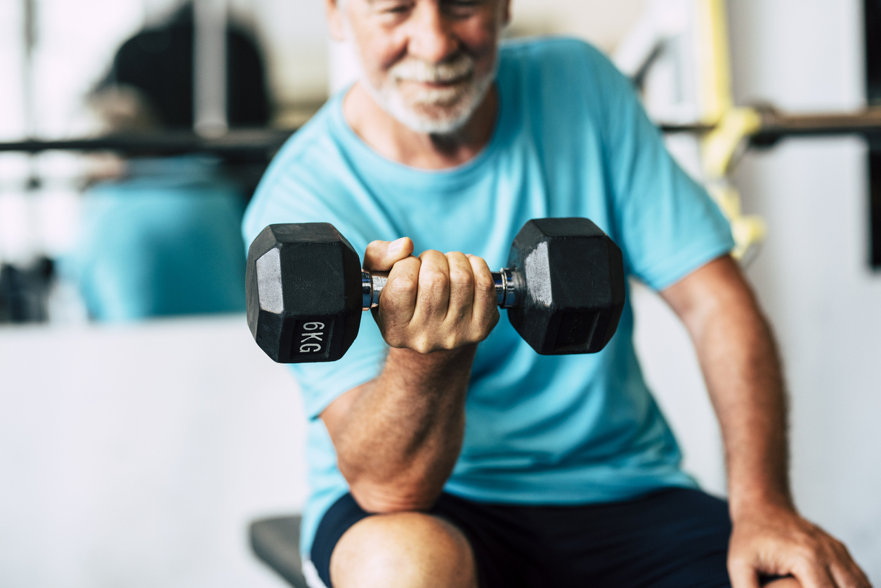 adult man and mature senior at the gym working his body with dumbbell - one man hapy training indoors sitted on the bench