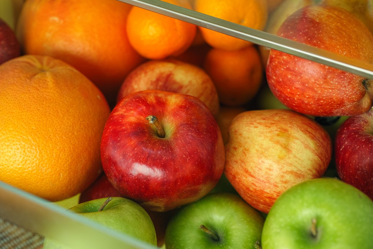 Organic apples and citrus fruits in a container from a fridge. Close up.