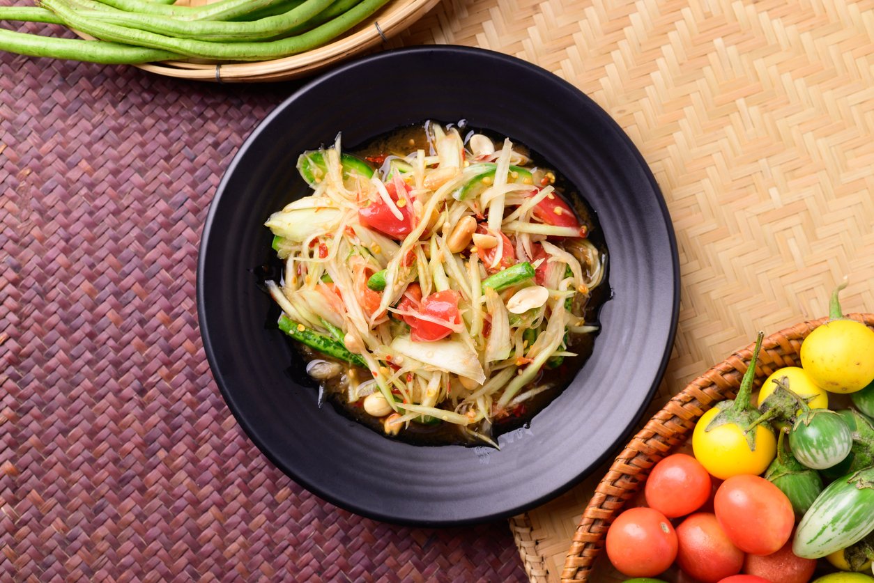 Thai food (Som tum), Spicy green papaya salad with vegetables on woven bamboo background