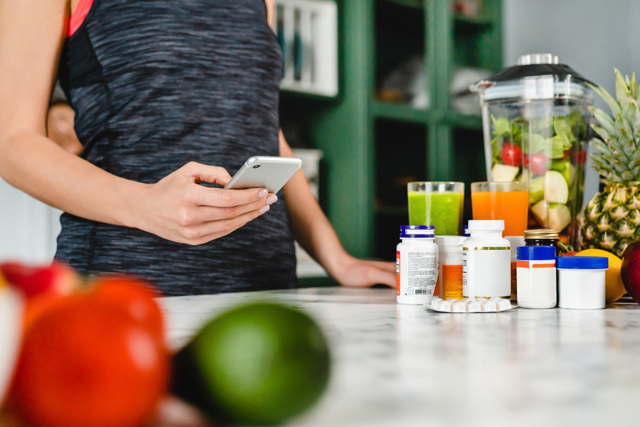 Young woman searching info about food supplements on her phone with fruits and additives on the table