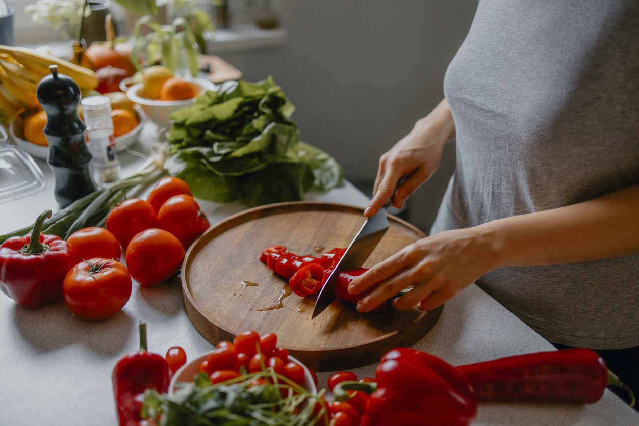 Cooking at home: an anonymous woman slicing peppers and tomatoes for a nutritious vegan lunch.