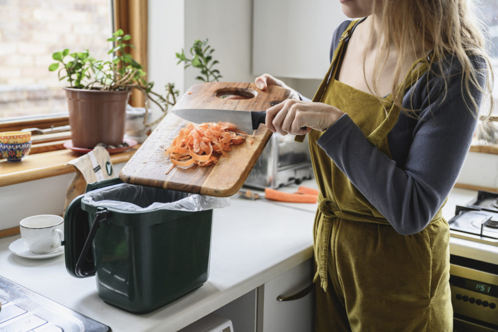 Woman in kitchen putting carrot scraps into countertop composter