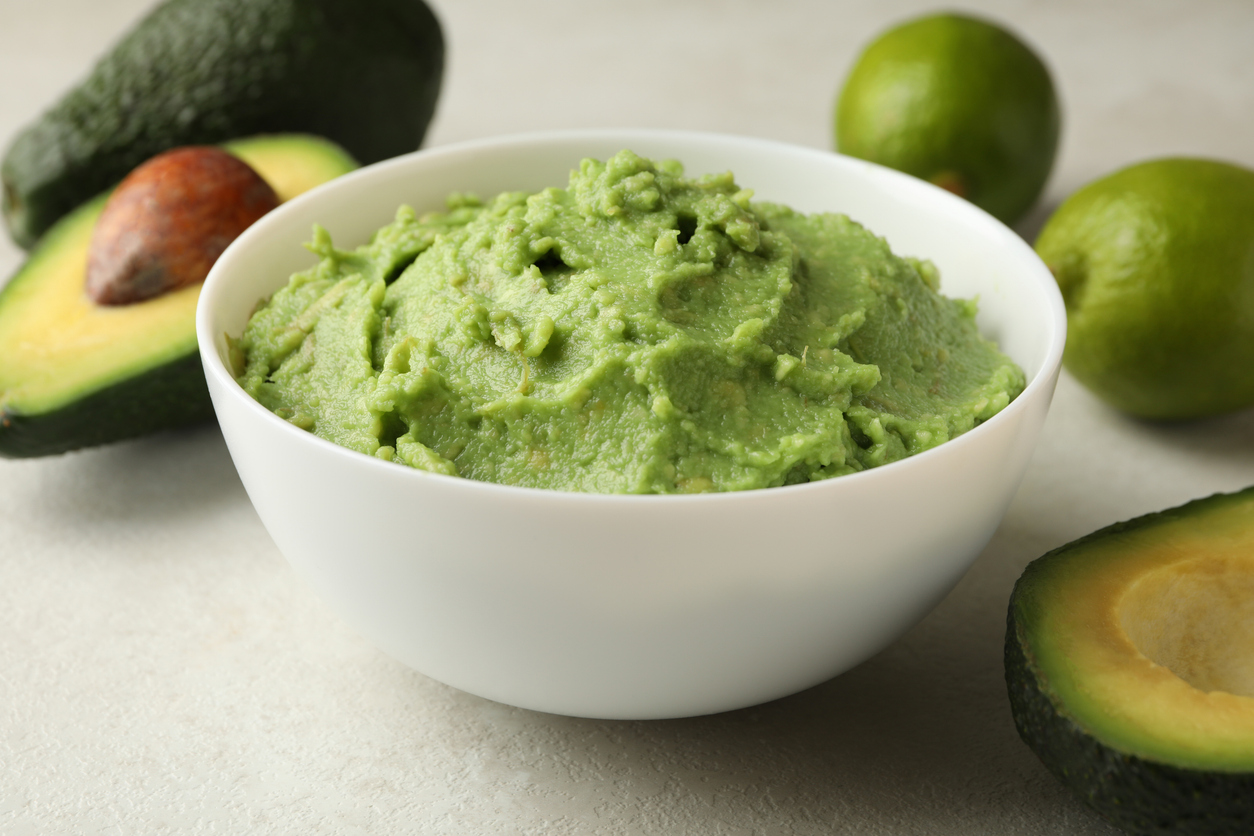 Bowl of guacamole, avocado and lime on white textured background, close up