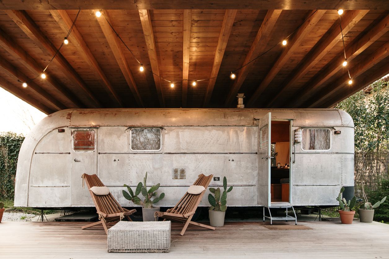 A restored american camper trailer with retro / vintage style. The camper trailer has been placed below a wooden porch