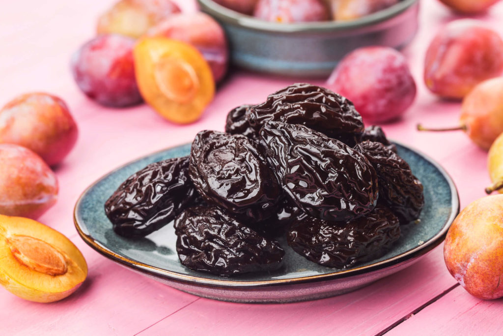 A plate of dried plums or prunes surrounded by fresh plums