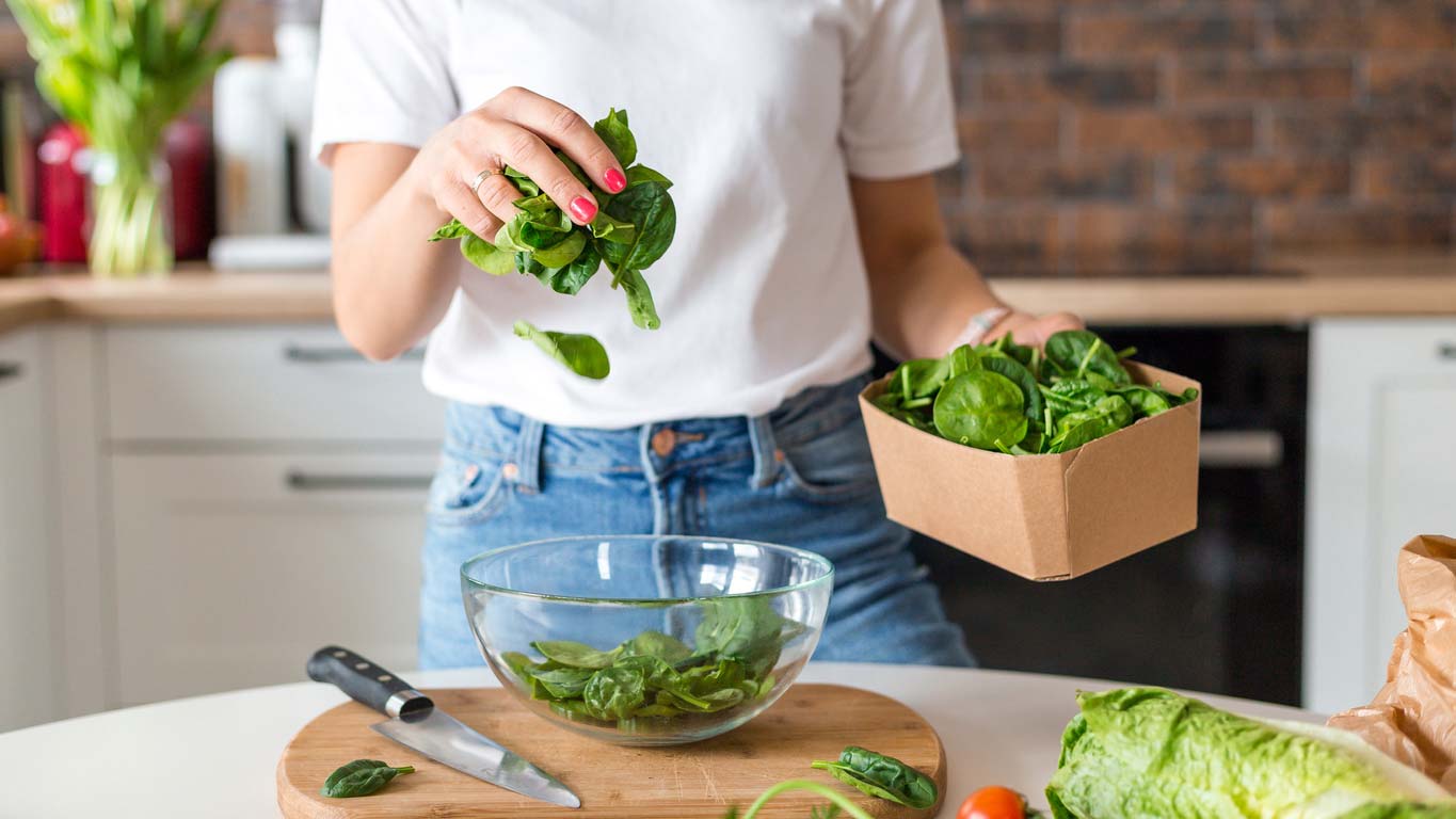 close up of woman in white shirt prepping spinach salad