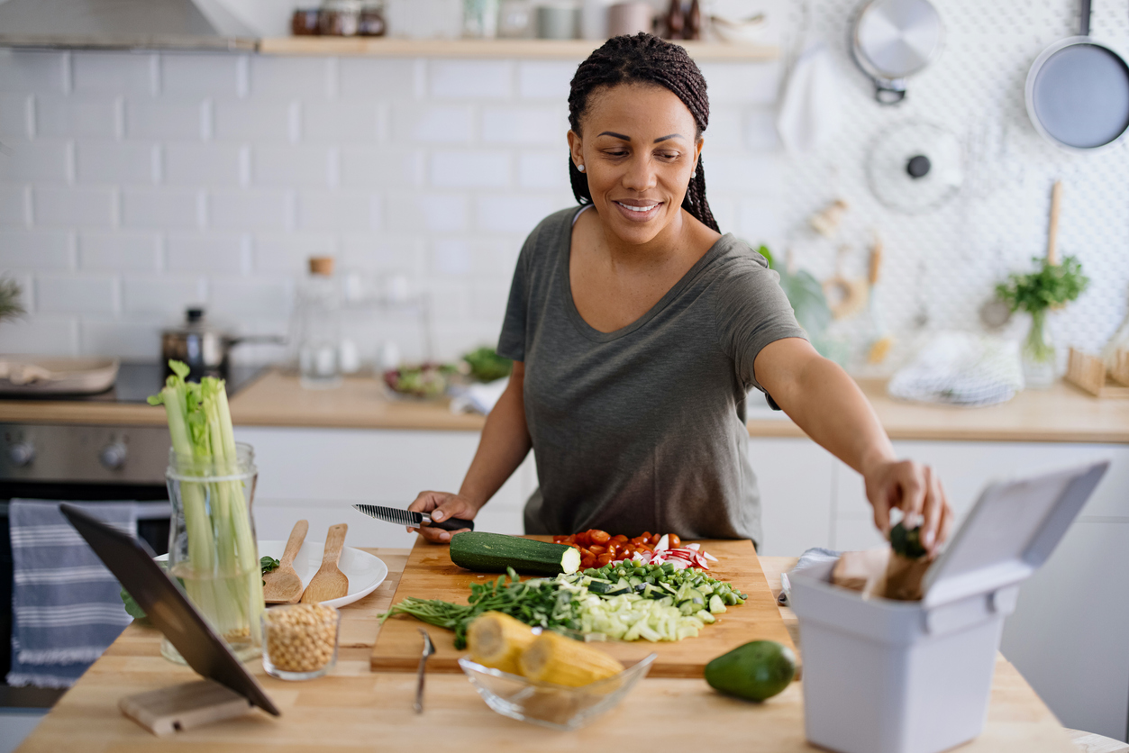 African woman preparing healthy vegetarian food. Cutting vegetables into small pieces. Summer chopped veggie salad