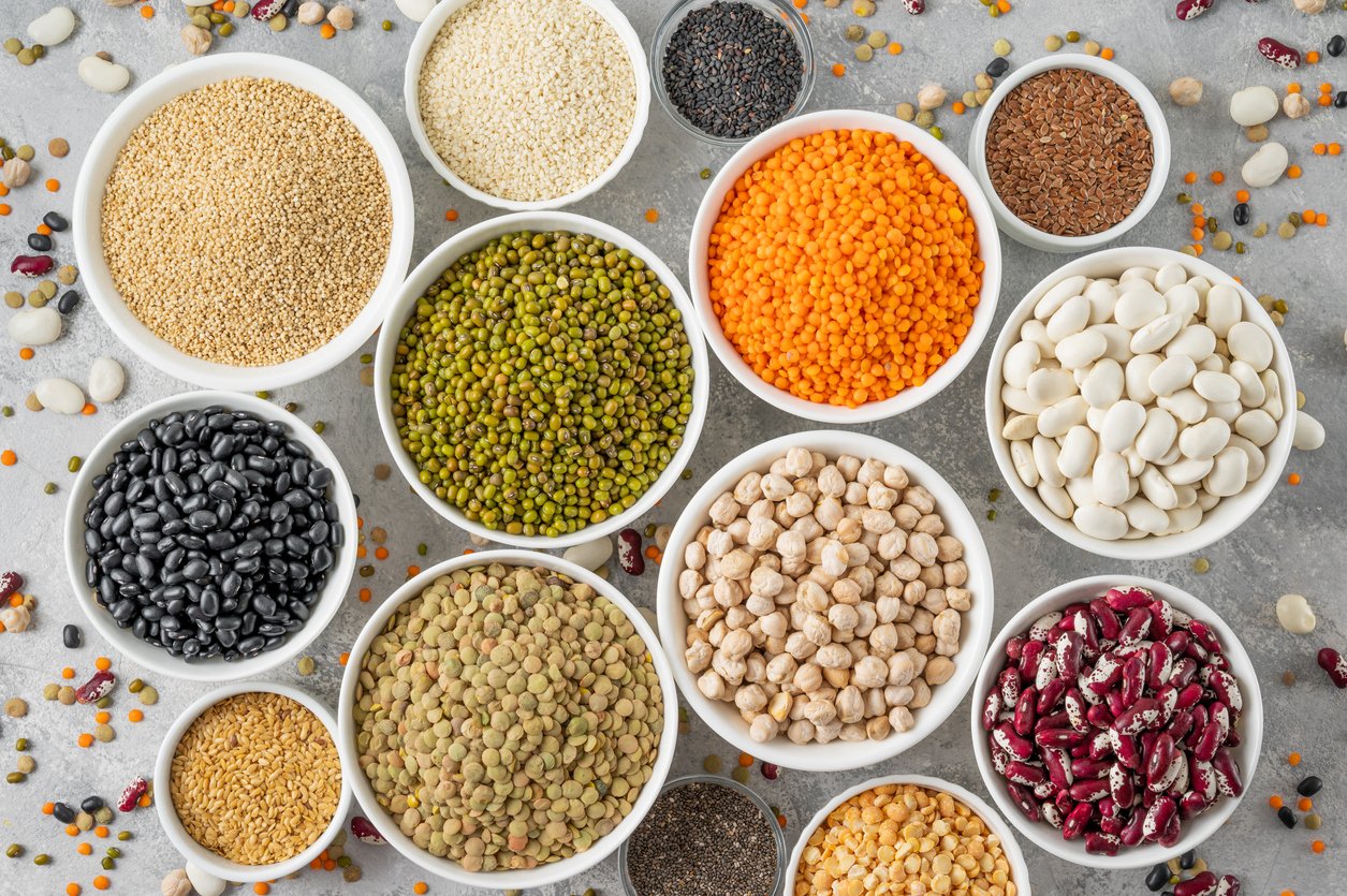 Mix of legumes, chickpeas, lentils, beans, peas, quinoa, sesame, chia, flax seeds in bowls on a gray concrete background. Healthy, vegan and gluten free food. Top view