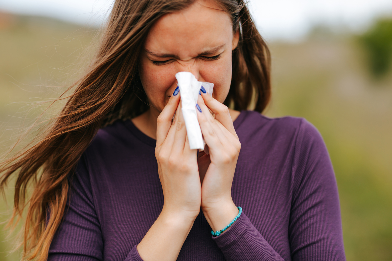 Woman with allergy symptom blowing nose and sneezing in paper tissue in nature