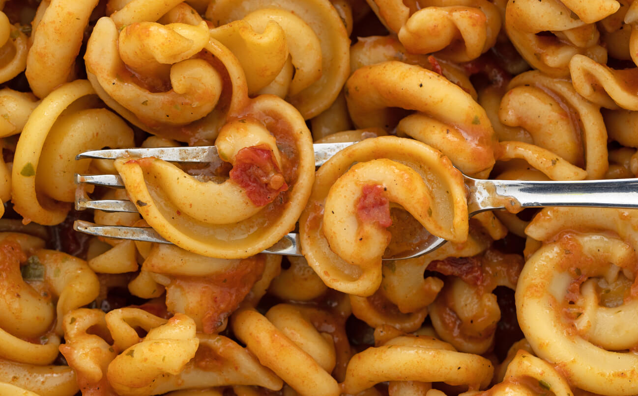 close view of pasta with tomatoes and seasonings with a fork in the food