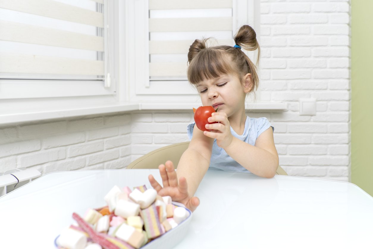 the little girl doesn't like the tomato, she reaches for a plate of sweets.