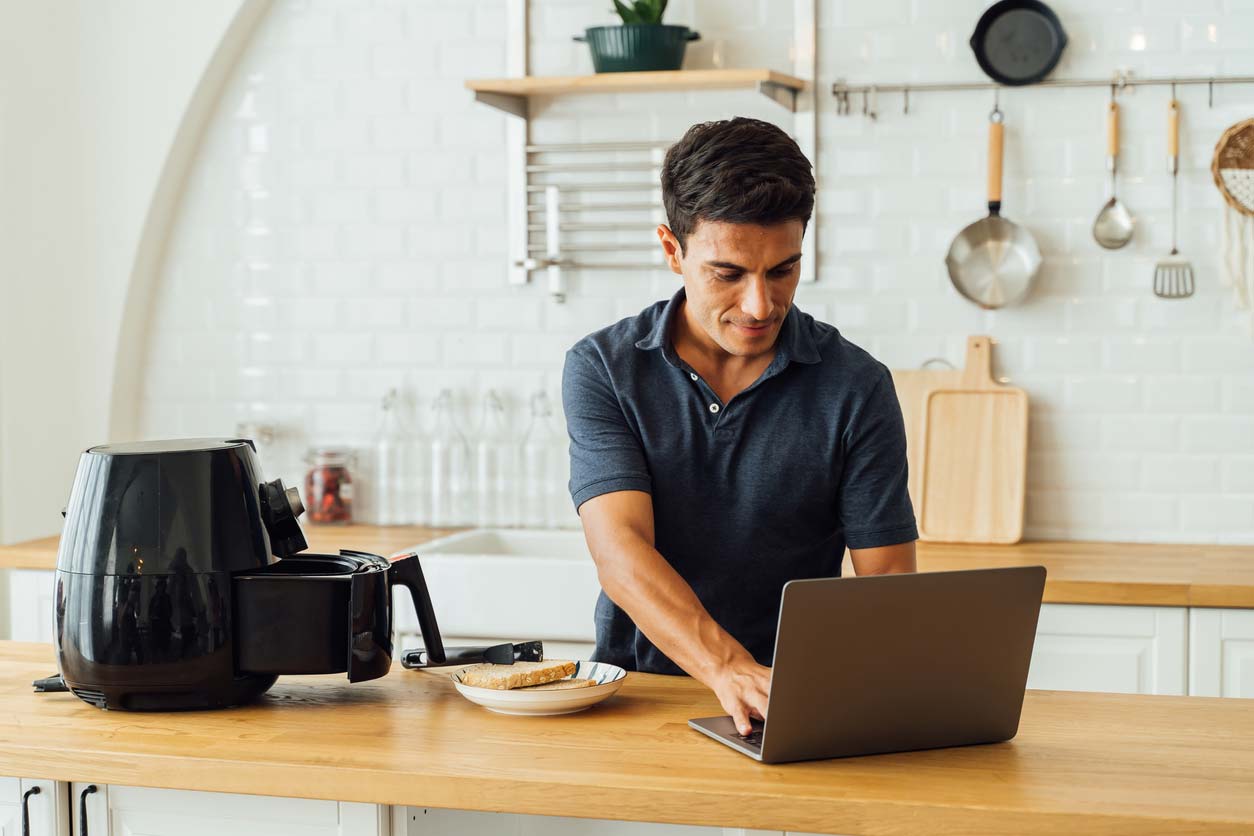 man using air fryer and laptop in kitchen