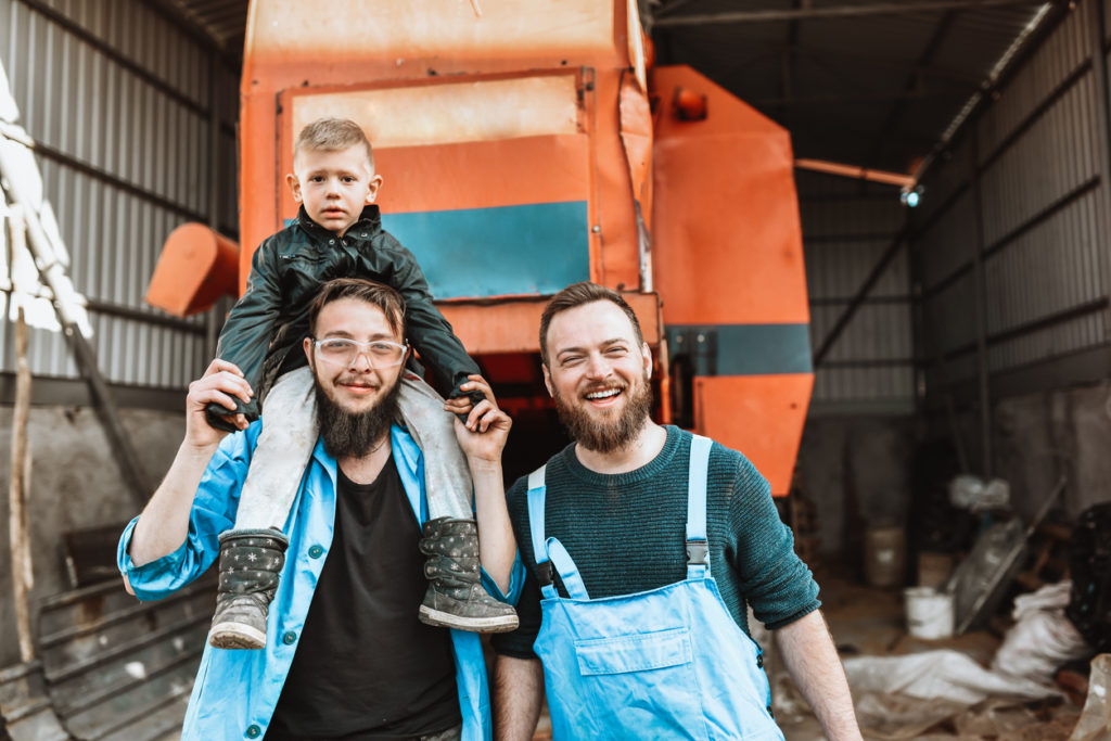 Queer farmers with their child in front of Harvester Machine