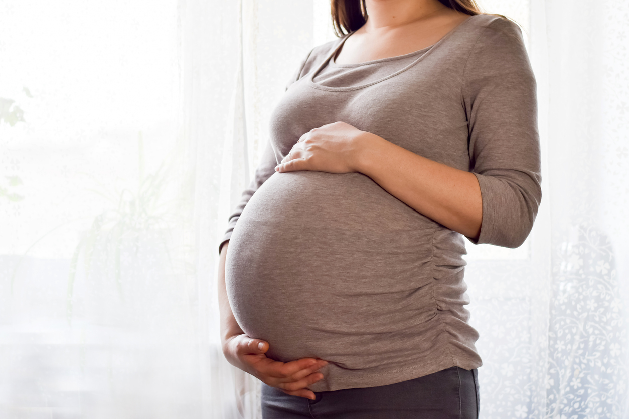 Pregnant woman with big belly at window. Maternity prenatal care and woman pregnancy concept. Young pregnant woman holds her hands on her swollen belly. Love concept. Horizontal with copy space.