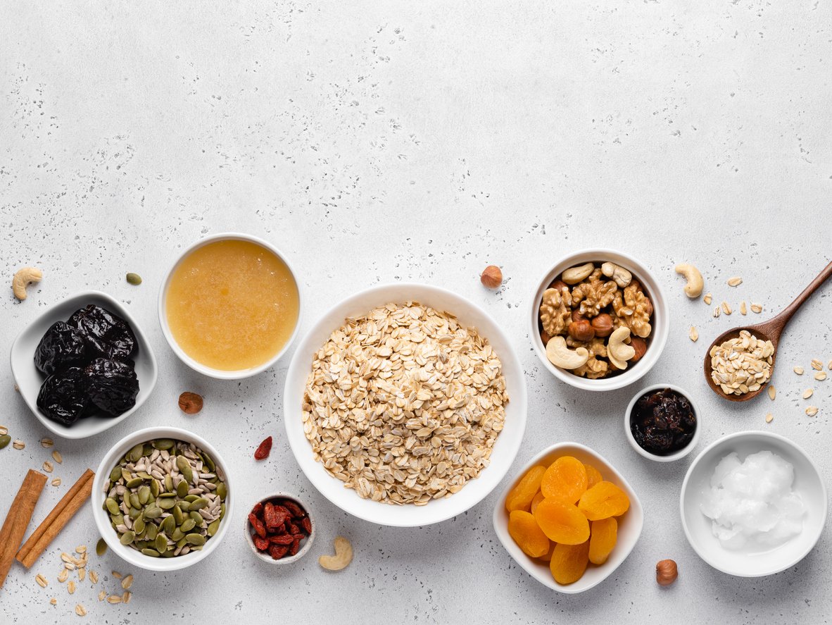 Granola ingredients top view. Oatmeal (flakes), nuts, seeds, prunes, dried apricots and berries, honey bowl. Grey concrete background.