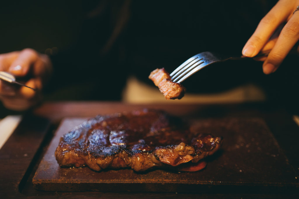 Close-up shot of hands cutting steak in a restaurant.
