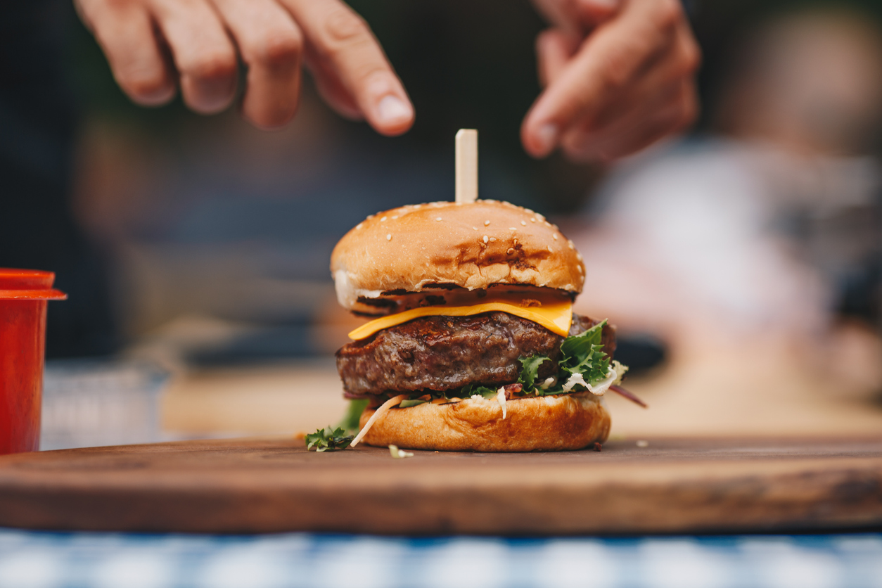 Homemade burger with lettuce and cheese on wooden chopping board. Preparing food outdoors. Chef making hamburger.