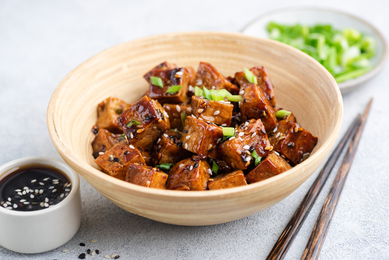 Tofu cubes in sweet teriyaki sauce with sesame seeds and scallions in bamboo bowl