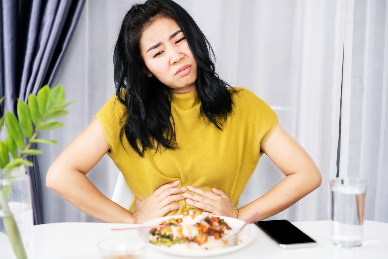 Asian woman suffering from stomachache, GERD after eating spicy food hand holding her pain stomach sitting at the table