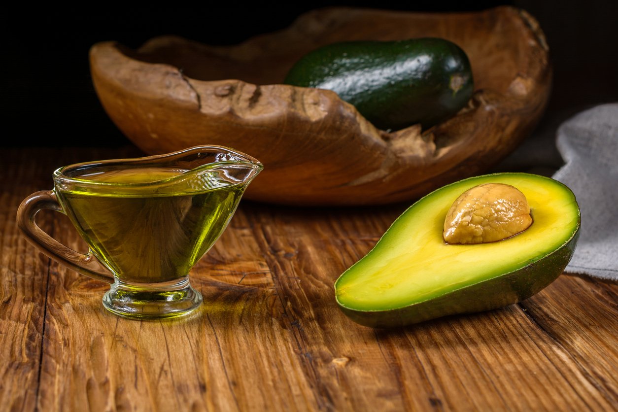 Half avocado fruit and avocado oil in a glass bowl on rustic table. Healthy eating, diet, body care and hair care concept.