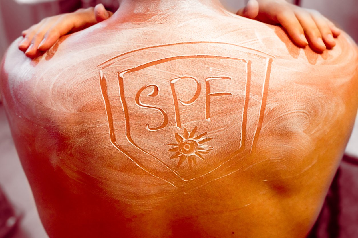 SPF, sun protection concept. Sunburn man back hands on shoulders. Applying Sun Cream in form of the sun and shield.