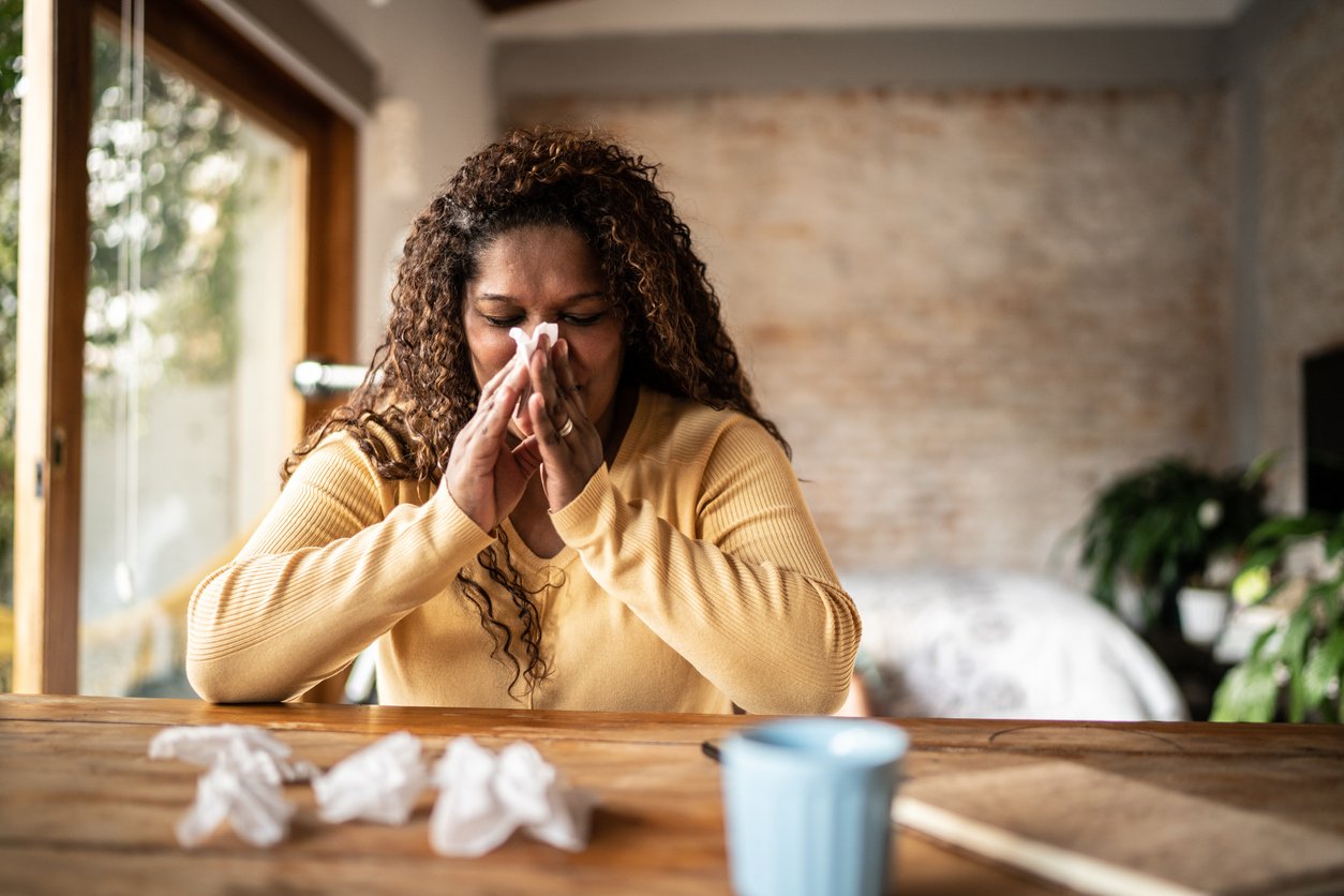 Sick mature woman of color blowing nose at home