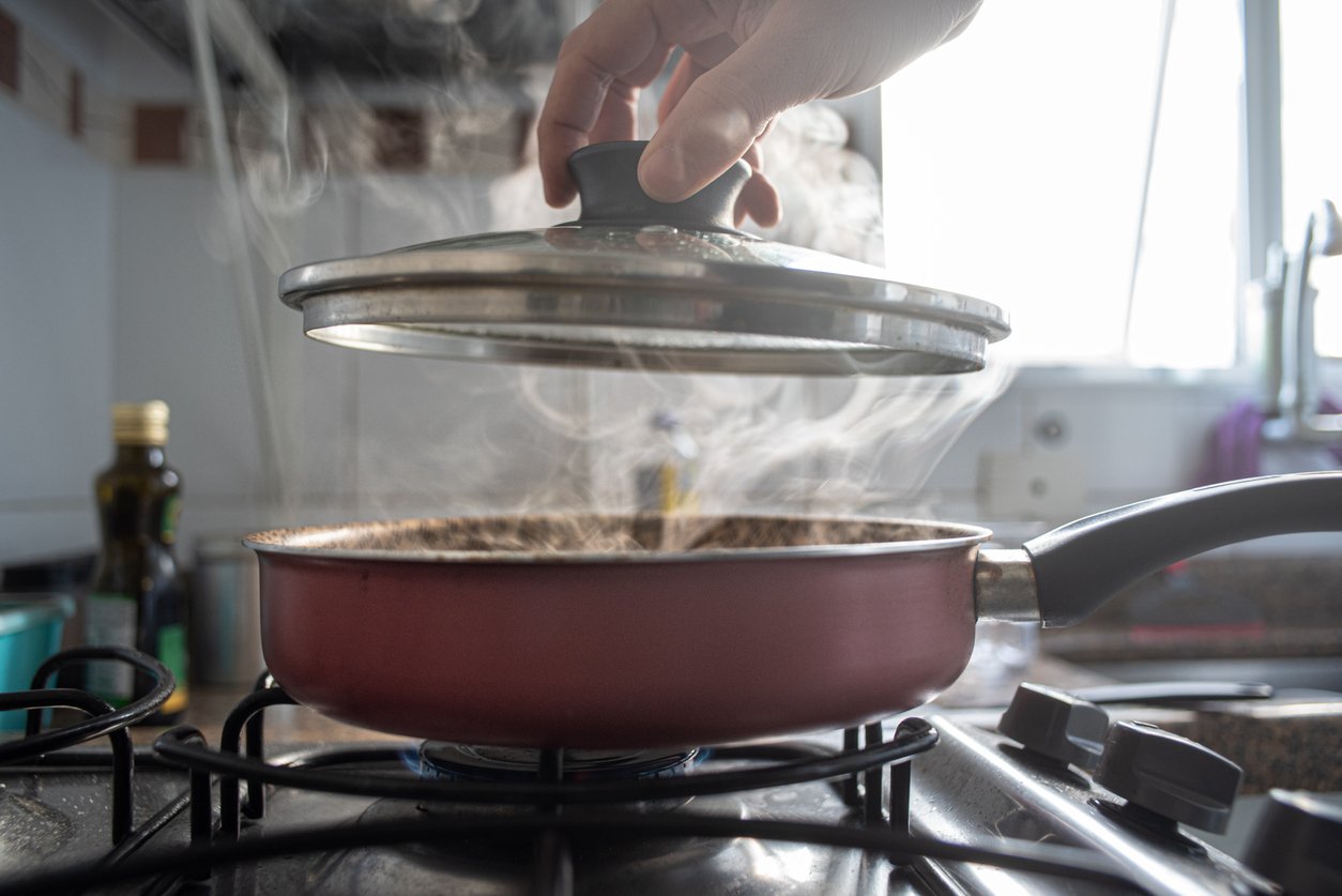 Detail of smoke coming out of a pot as a man opens the lid while cooking at home.