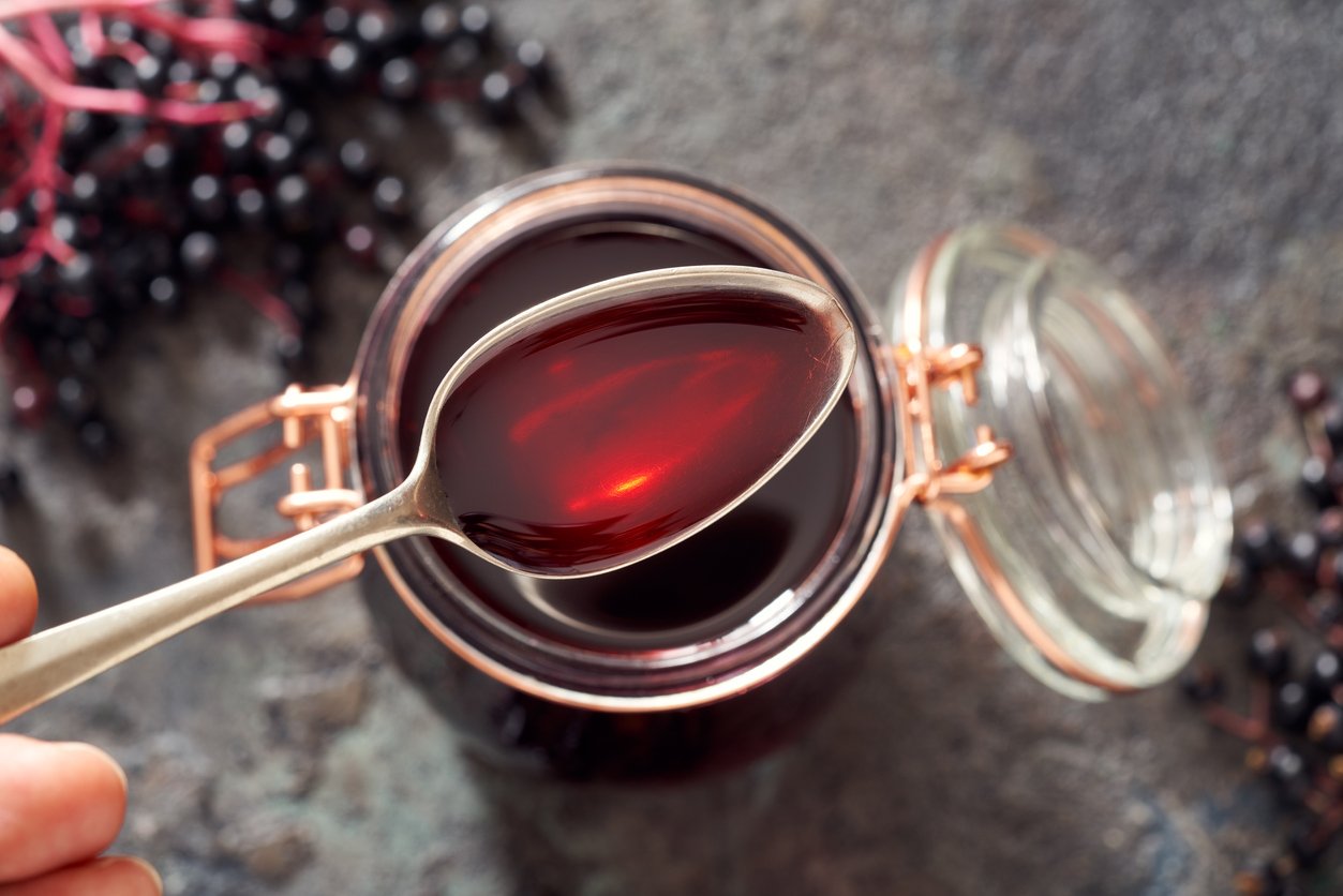 Spoon with homemade black elder syrup, with fresh elderberries