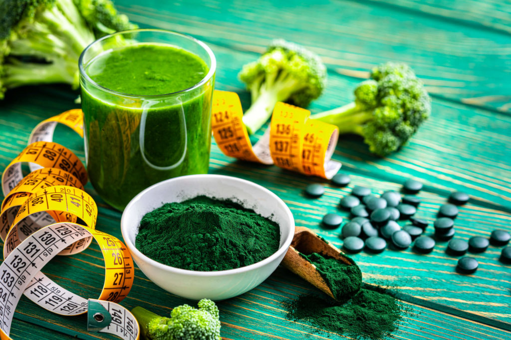 Green powders and supplements surrounded by broccoli and a tape measure