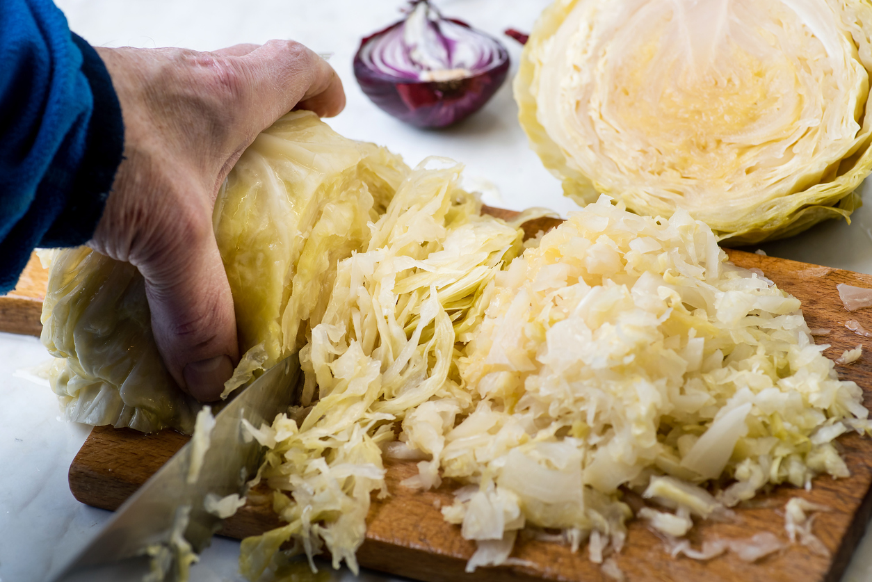 Male hand slicing sour cabbage on a cutting board