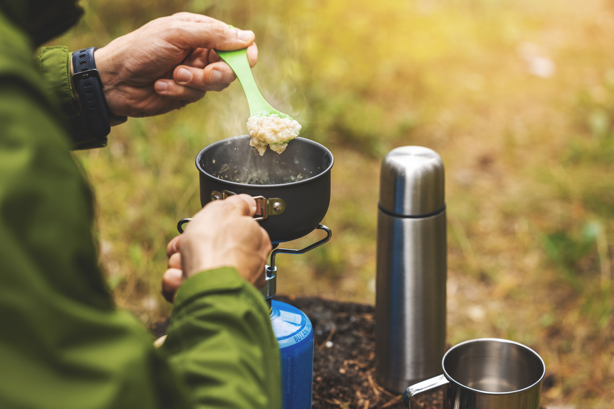 preparing oatmeal porridge outdoors on gas burner. camping cooking equipment