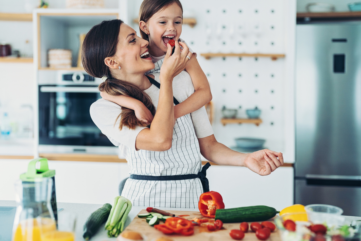 Smiling mother and little daughter preparing salad together