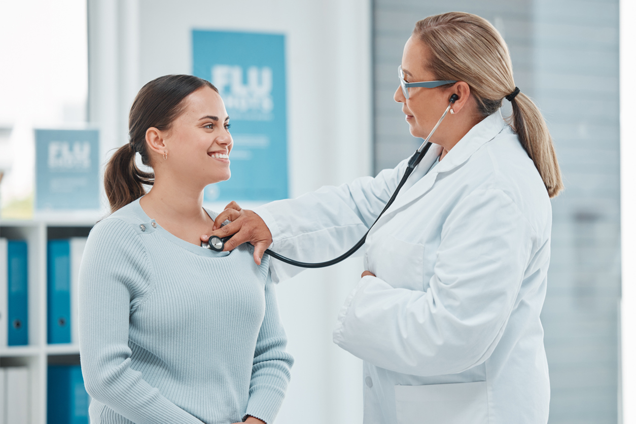 Female doctor listening to the heart of a smiling young woman