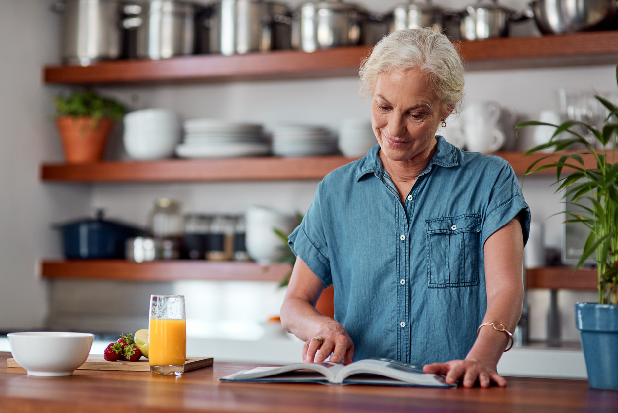 Shot of a mature woman reading a book while preparing breakfast at home