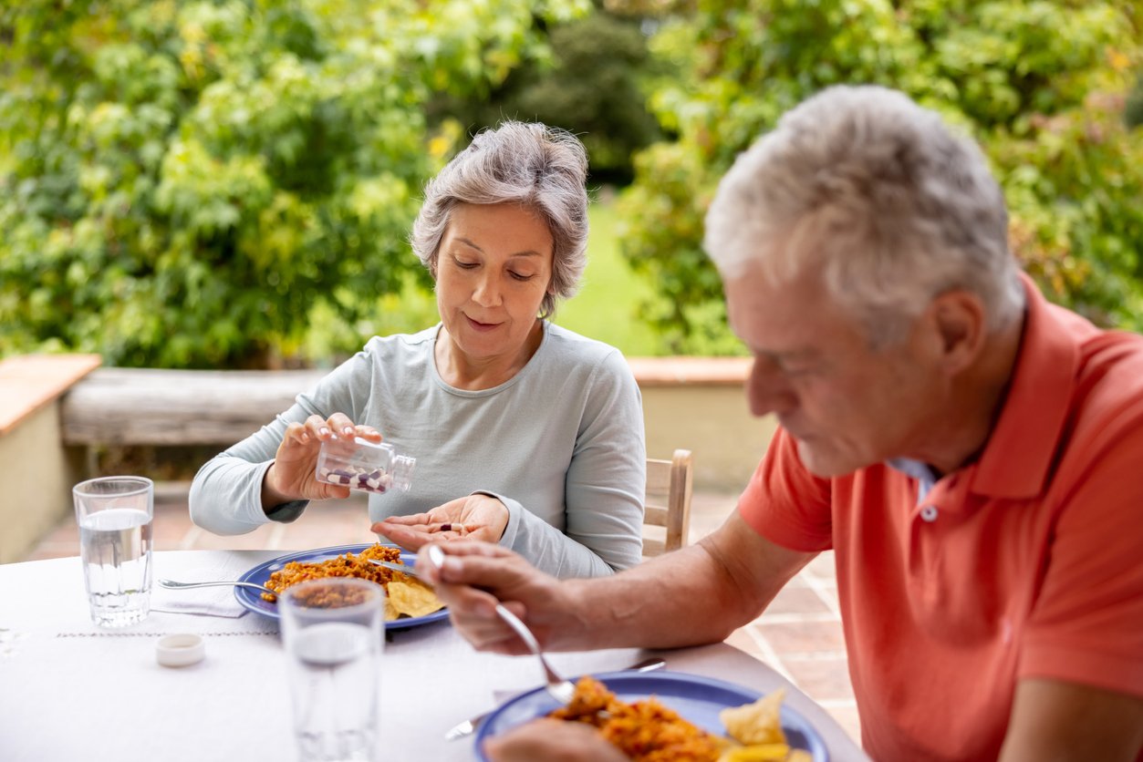 Latin American senior woman at home taking her medicine while eating outdoors - healthcare and medicine concepts