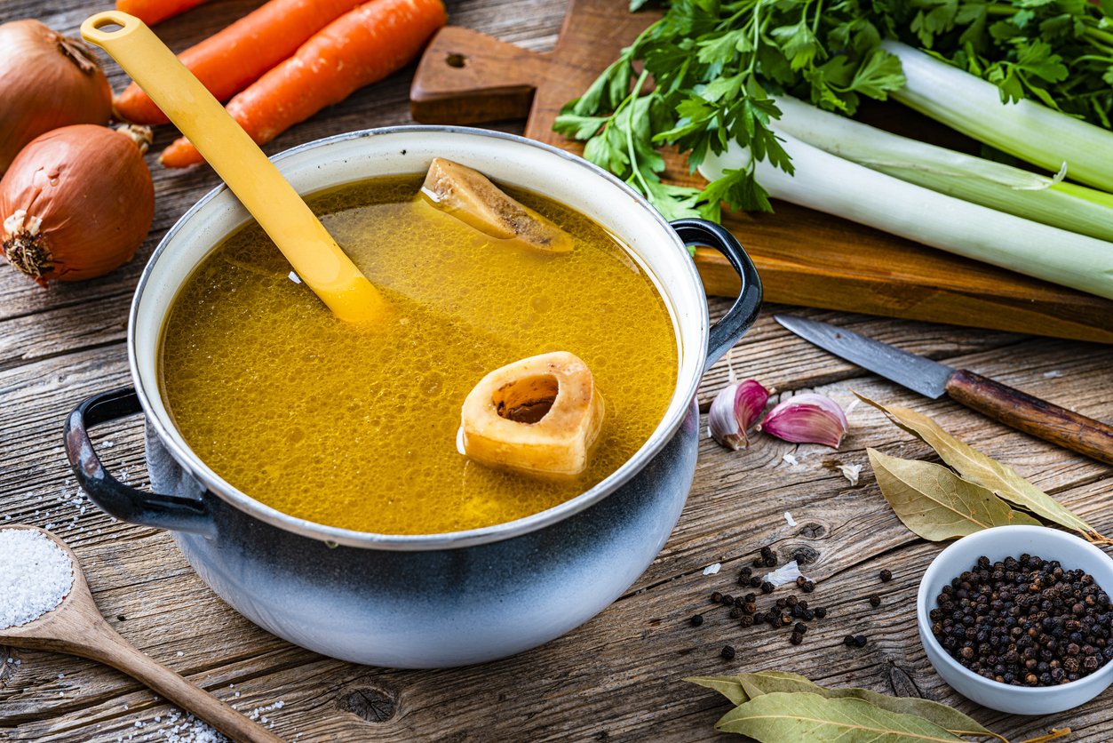 High angle view of a cooking pan filled with homemade bone broth shot on rustic wooden table. Ingredients for cooking bone broth are all around the pan. High resolution 42Mp studio digital capture taken with Sony A7rII and Sony FE 90mm f2.8 macro G OSS lens