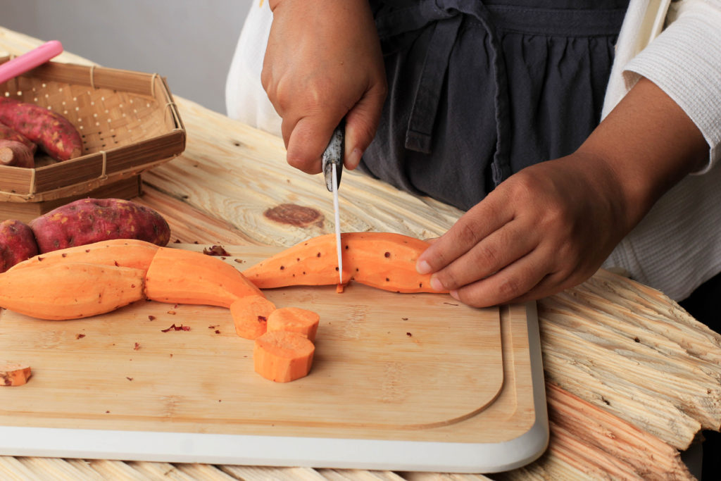 Hands cutting sweet potatoes on a cutting board in the kitchen