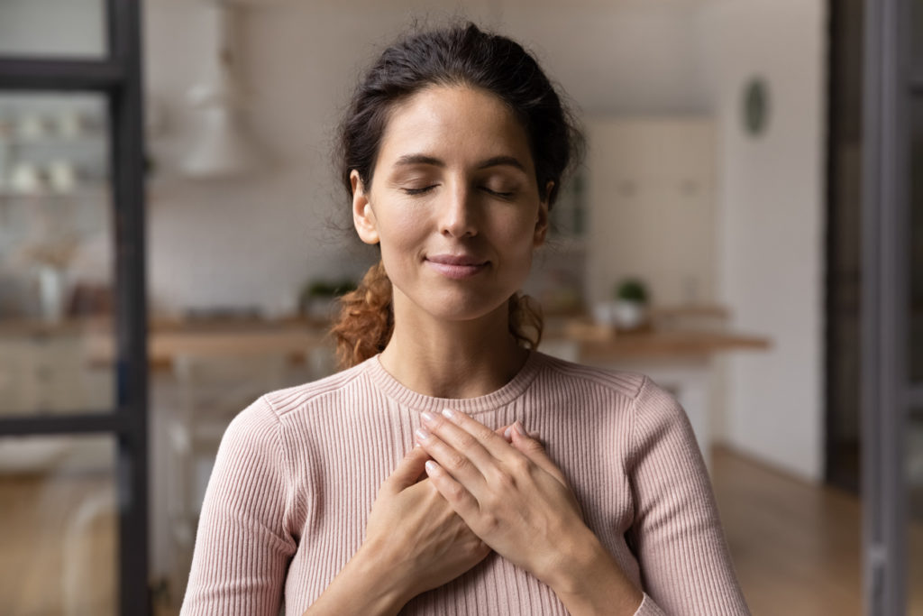Woman with eyes closed holding hands over heart in gratitude