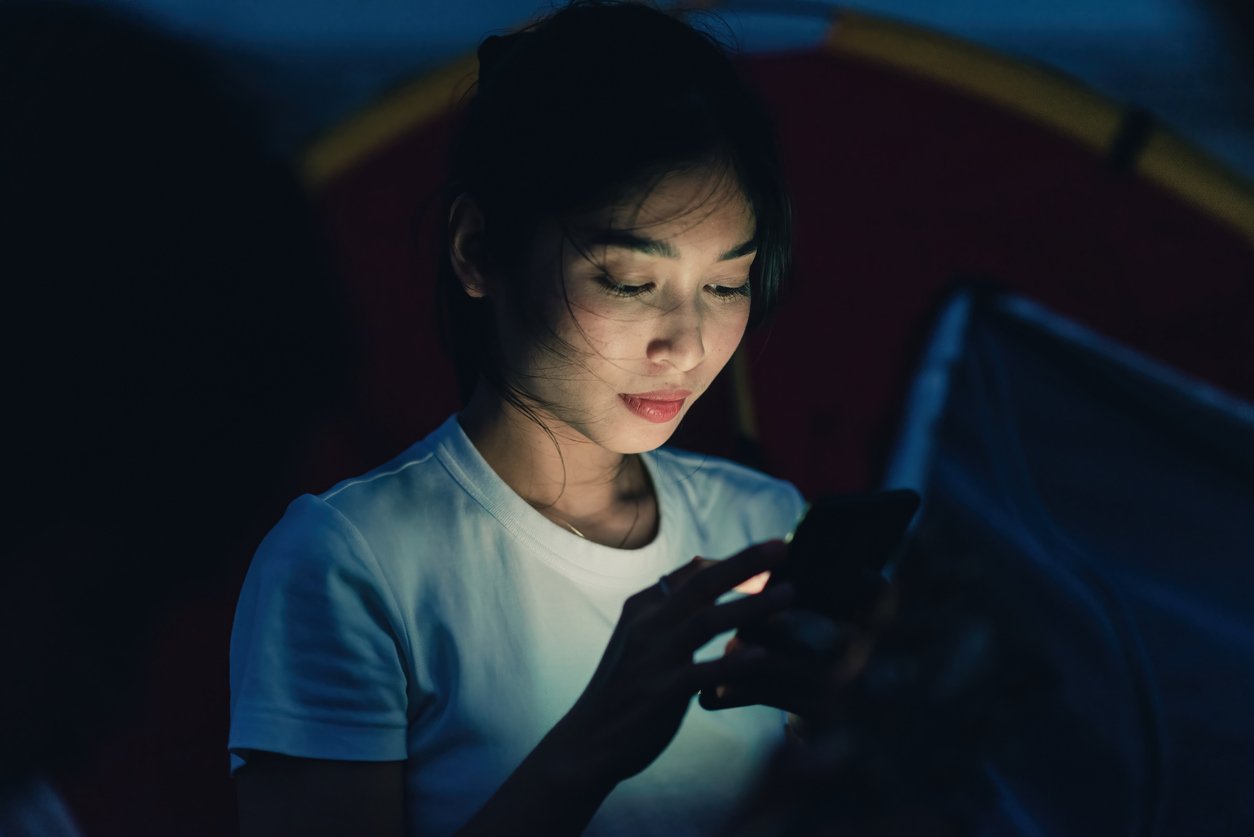 Concept blue light from smartphone screen, Asian woman using smartphone with bright light from screen under low light and dark conditions.