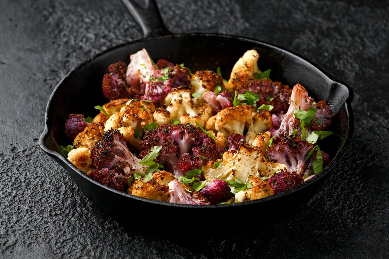 Roasted purple, white cauliflower with herbs on cast iron pan.