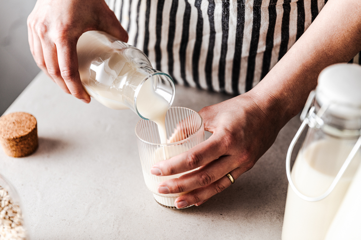 Close-up of a female pouring freshly made oat milk in a glass. Woman serving healthy oat milk.
