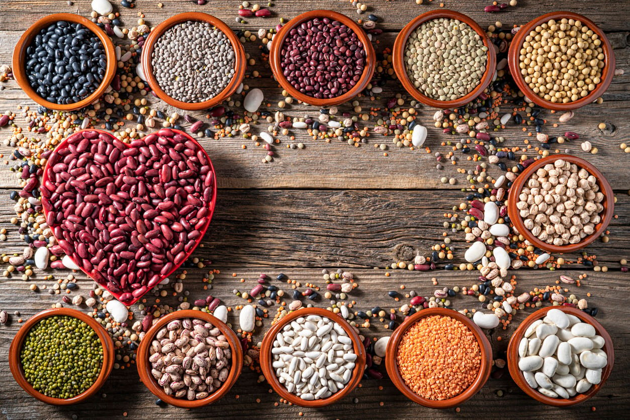 assorted legumes in pottery bowls with red heart on rustic wooden background frame